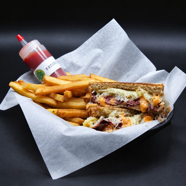 Toasted Reuben sandwich with melted cheese, sauerkraut, and fries, served with ketchup.