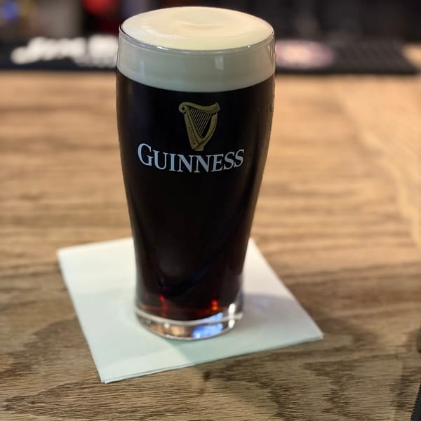 A pint of Guinness beer with a creamy head on a white napkin on a wooden bar.
