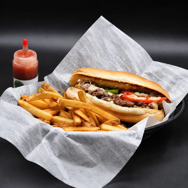 Cheesesteak sandwich with peppers and melted cheese, served with golden fries and hot sauce.